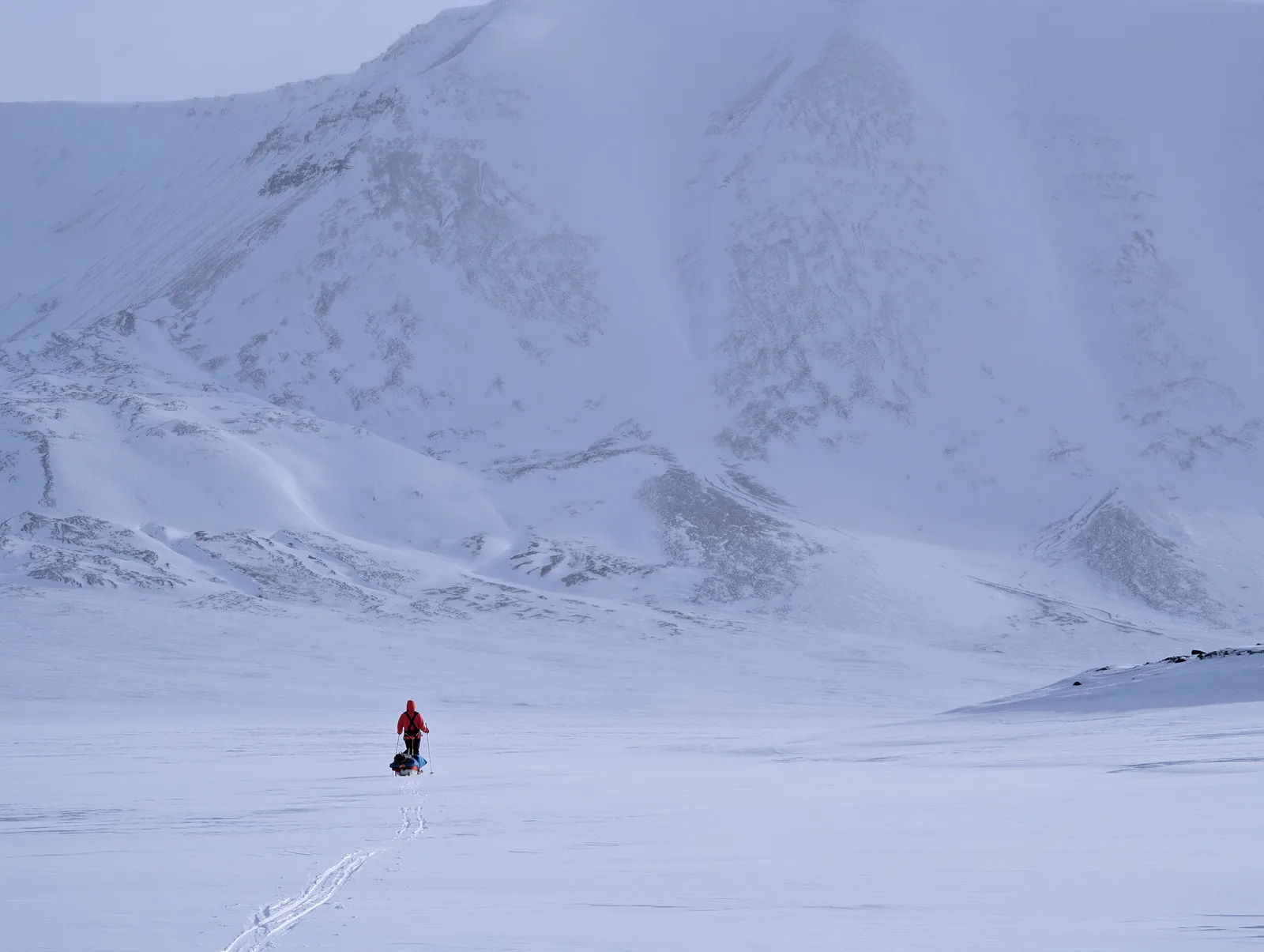A lone figure hauling a pulk across the width of the valley