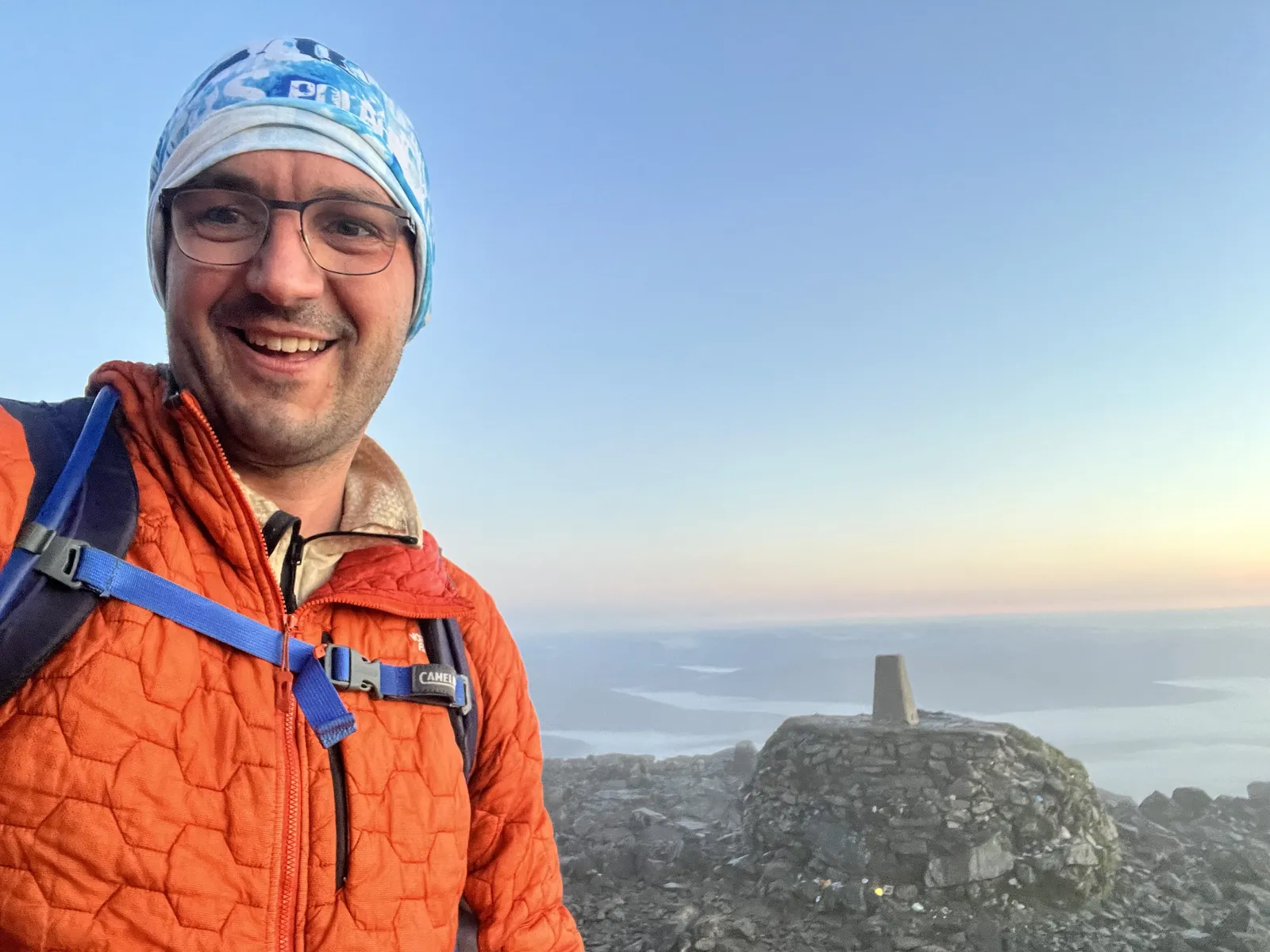 The summit of Ben Nevis at first light, ThermoBall on over a soaked base layer, the fog sea behind.